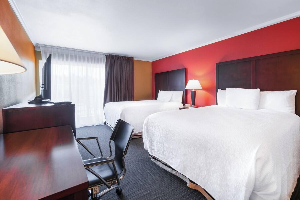 A hotel room with two beds, a desk, a chair, a TV, and a window with curtains.