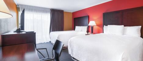 Une chambre d’hôtel avec deux lits, un bureau, une chaise, une télévision et une fenêtre avec des rideaux.