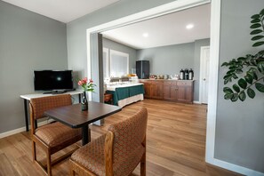 A dining area with a table and chairs, a television, and a kitchen in the background.