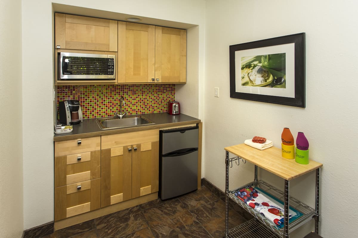 A compact kitchen with wooden cabinets, a stainless steel microwave, a dishwasher, and a tiled backsplash.