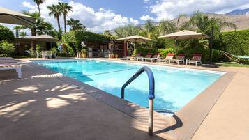 A swimming pool with lounge chairs and umbrellas, surrounded by palm trees and a mountain view.