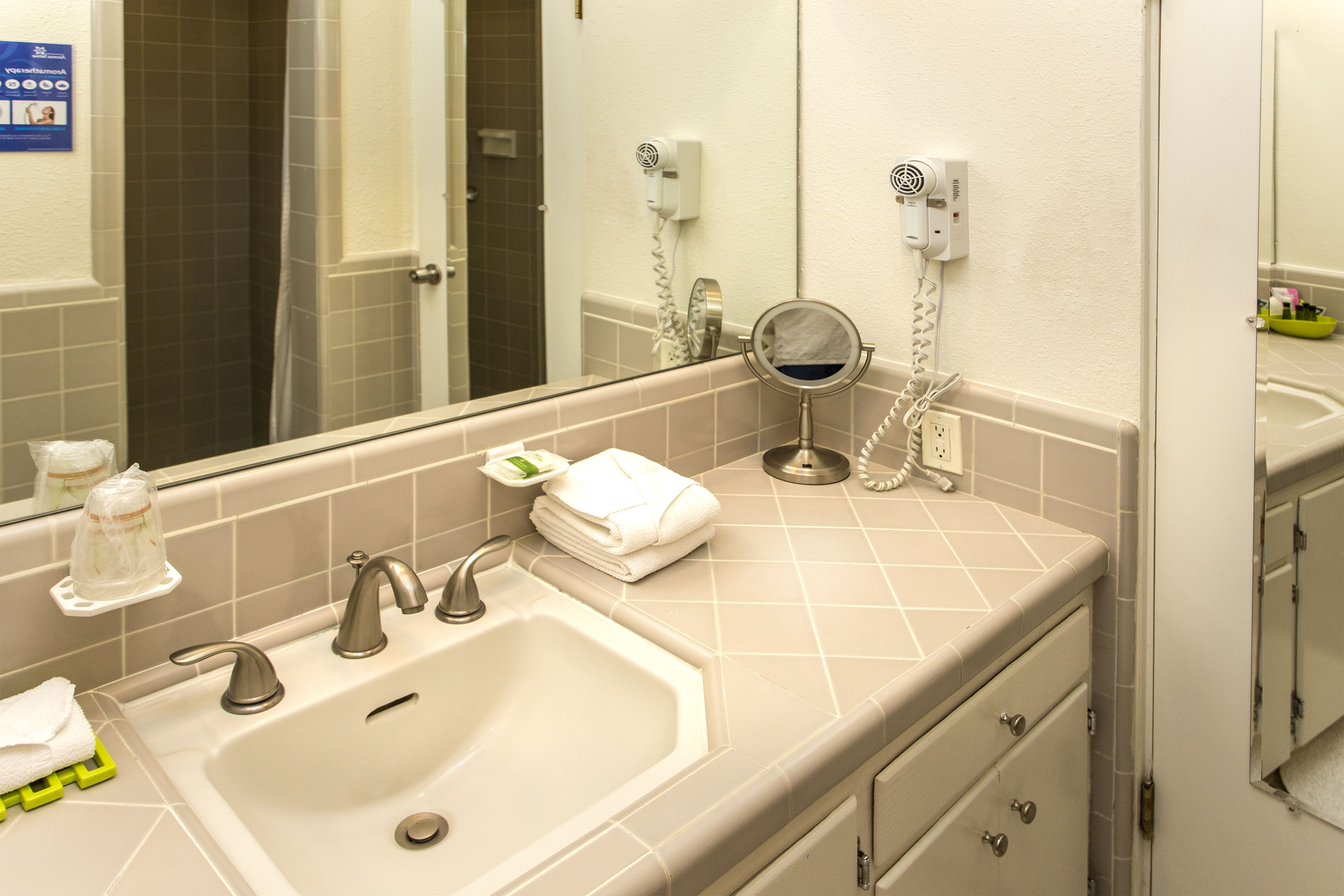 A bathroom with a sink, two faucets, a mirror, a towel rack, and a hairdryer on the wall.