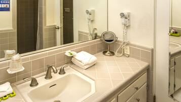 A bathroom with a sink, two faucets, a mirror, a towel rack, and a hairdryer on the wall.