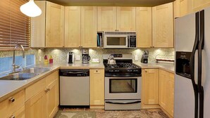 A compact kitchen with wooden cabinets, a microwave, a stove, a dishwasher, and a refrigerator.