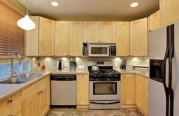 A compact kitchen with wooden cabinets, a microwave, a stove, a dishwasher, and a refrigerator. - Desert Riviera Hotel (Palm Springs)