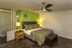 A bedroom with a bed, bedside lamps, a bench, a ceiling fan, and a radiator.