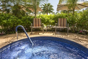 A swimming pool with a metal ladder, surrounded by palm trees and chairs with striped upholstery.
