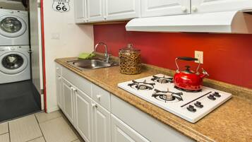 A compact kitchen with a gas stove, a red kettle, a jar of spaghetti, and a washing machine in the background.