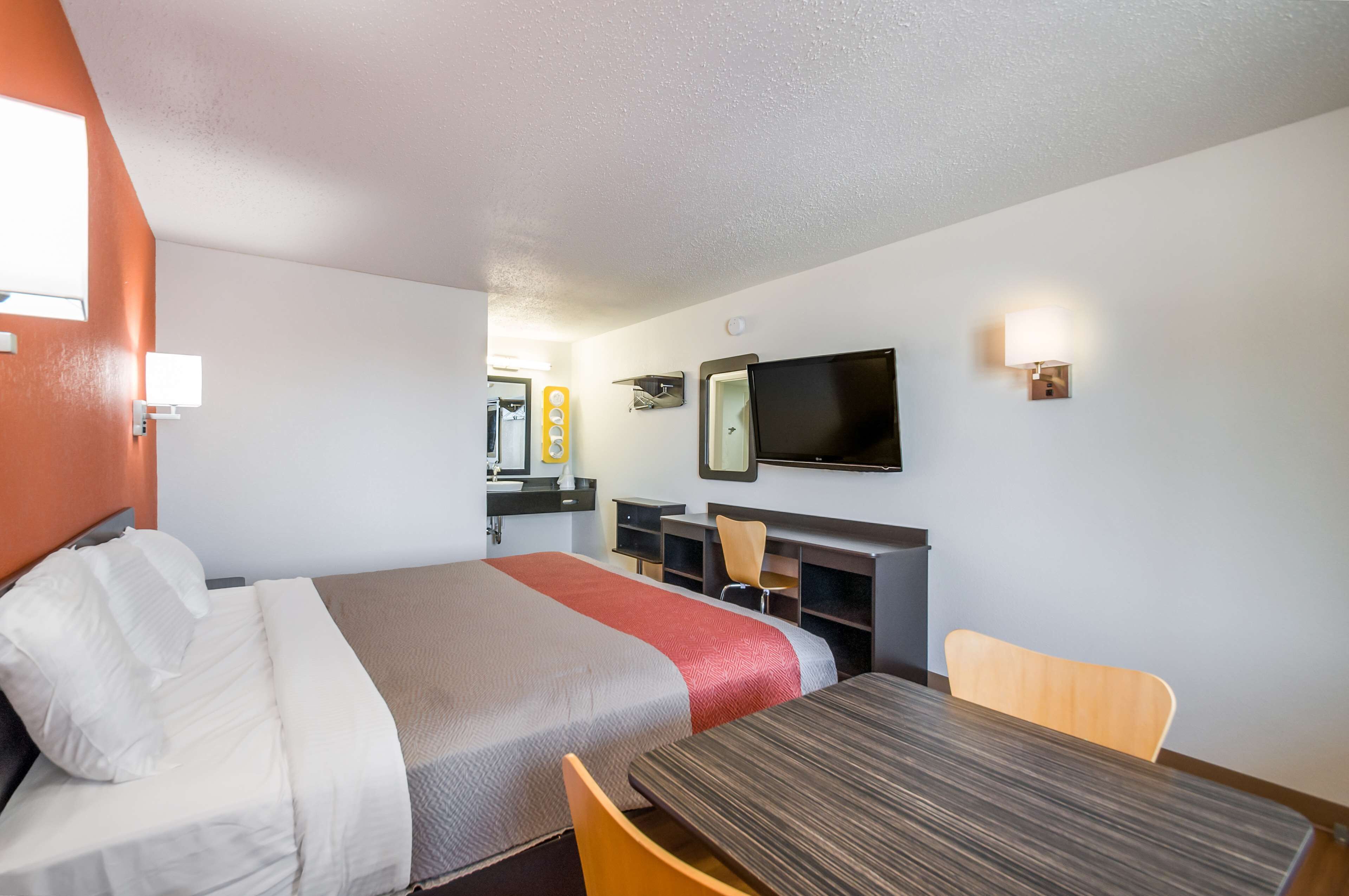 A hotel room with a bed, a desk, a chair, a TV, and a small kitchenette.