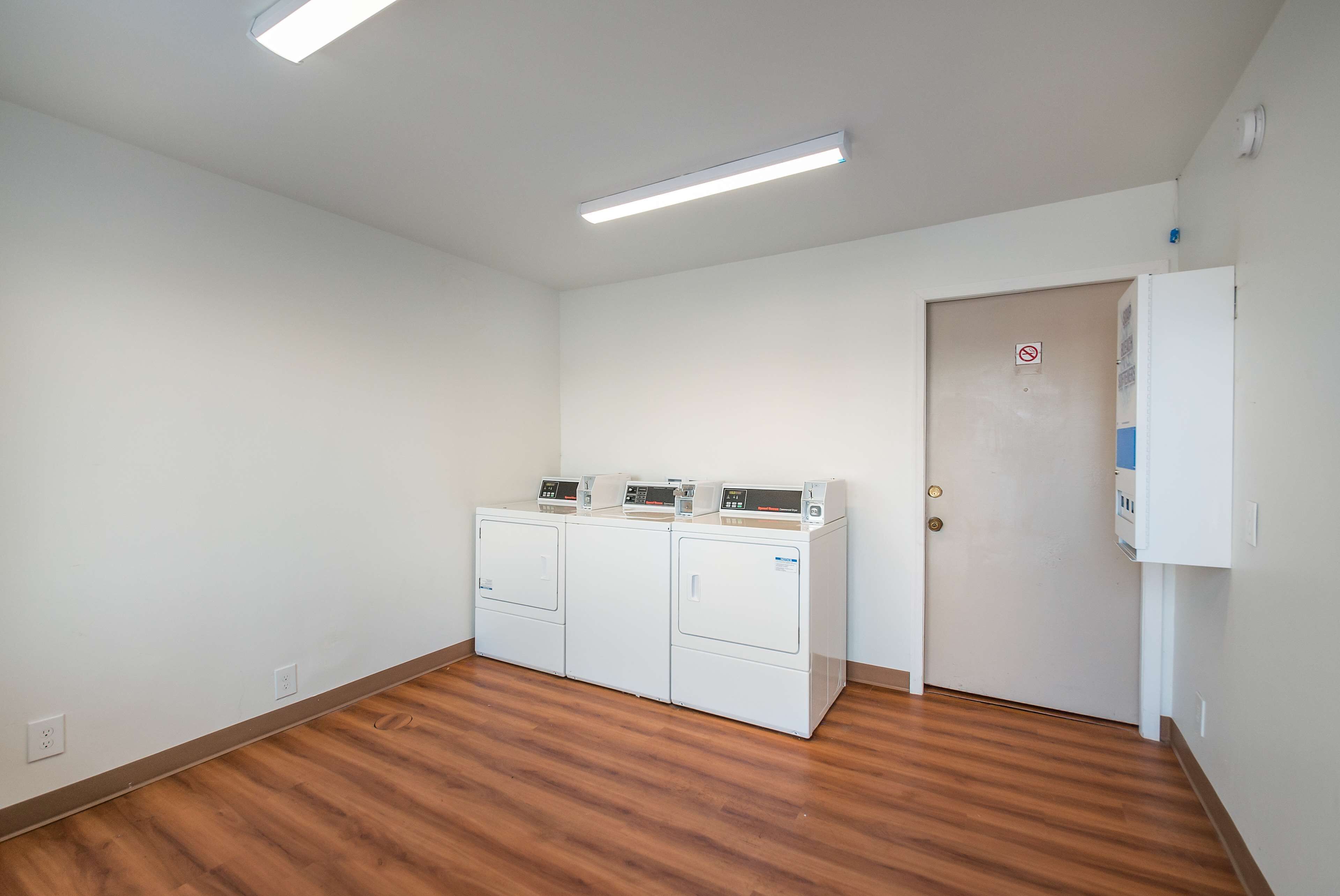 A laundry room with three stacked washers and dryers, a door with a no-smoking sign, and a white wall with a thermostat.