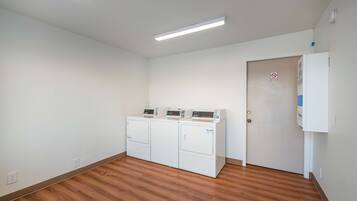 A laundry room with three stacked washers and dryers, a door with a no-smoking sign, and a white wall with a thermostat.