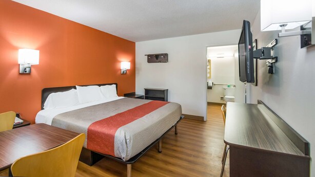 Ein Hotelzimmer mit einem Bett, einem Schreibtisch, einem Sessel, einem an der Wand montierten Fernseher und einem kleinen Tisch.
