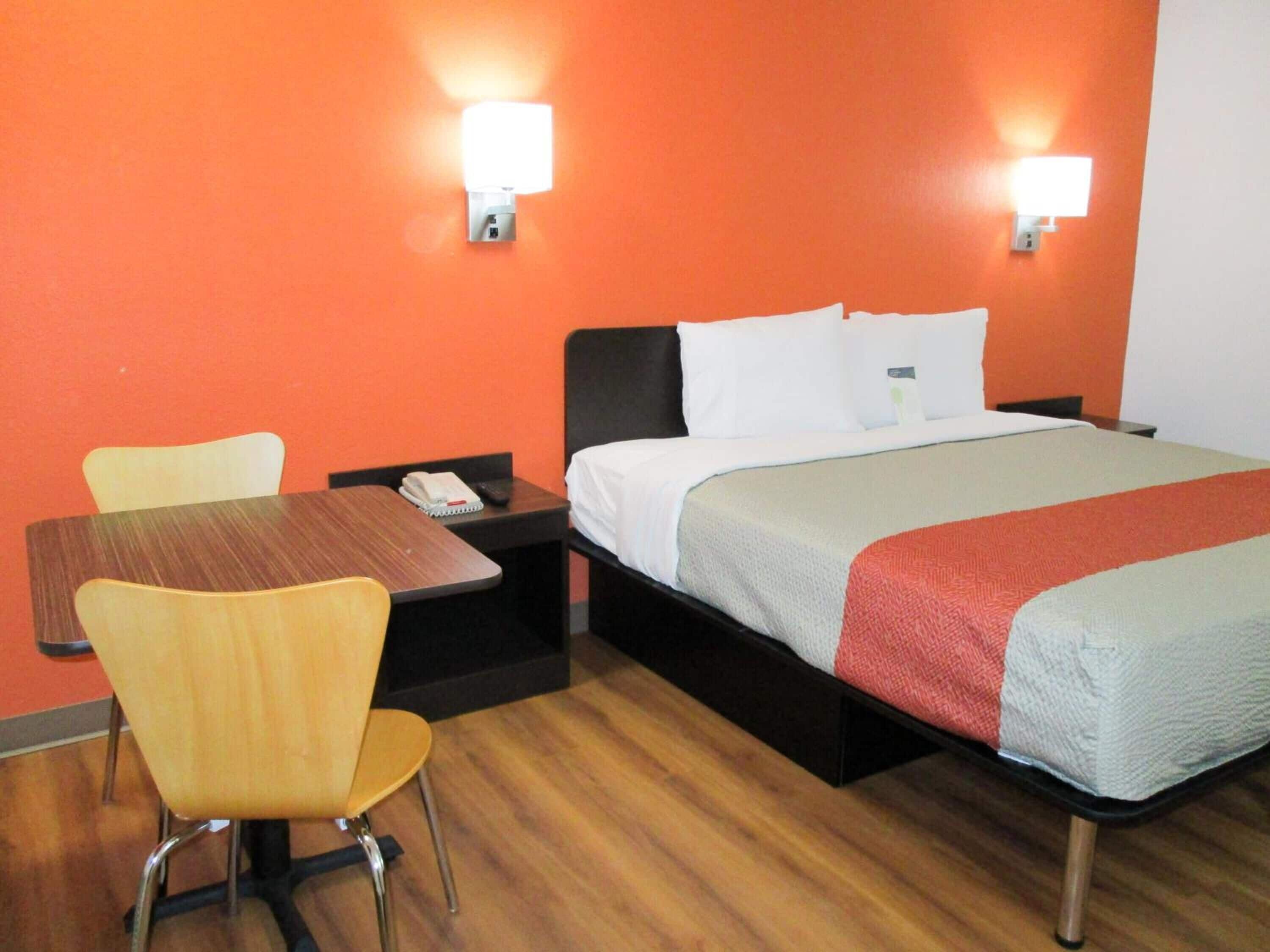 Una camera d'albergo con un letto, una scrivania, una sedia e due luci fissate alla parete.
