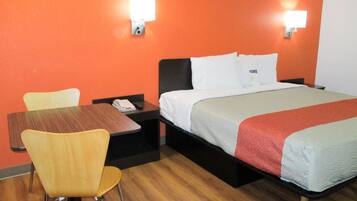 Una camera d'albergo con un letto, una scrivania, una sedia e due luci fissate alla parete.