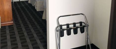 Una habitación de hotel con cama, escritorio, silla, perchero y ventana con cortinas.