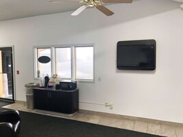 A room with a black entertainment unit, a ceiling fan, a large window, and a wall-mounted TV.