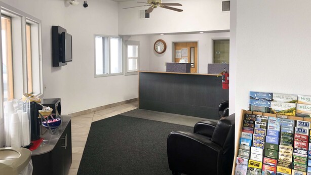 A reception area with a reception desk, a clock, and a fire extinguisher. There are two windows and a ceiling fan.