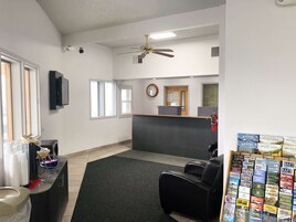 A reception area with a reception desk, a clock, and a fire extinguisher. There are two windows and a ceiling fan.