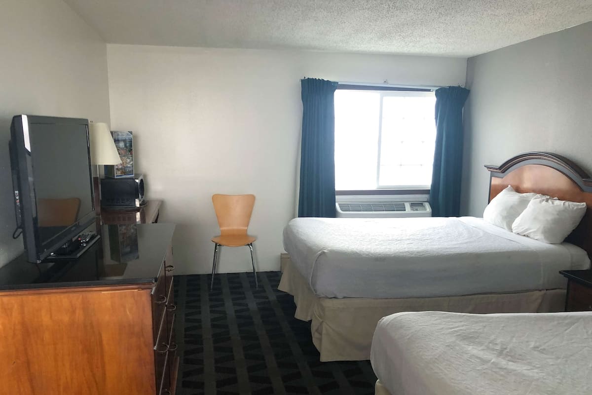 A hotel room with a bed, a chair, a desk with a television, and an air conditioning unit.