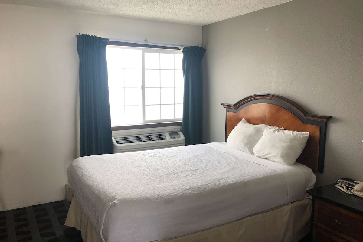 A hotel room with a bed, a bedside table, a phone, and a window with curtains.