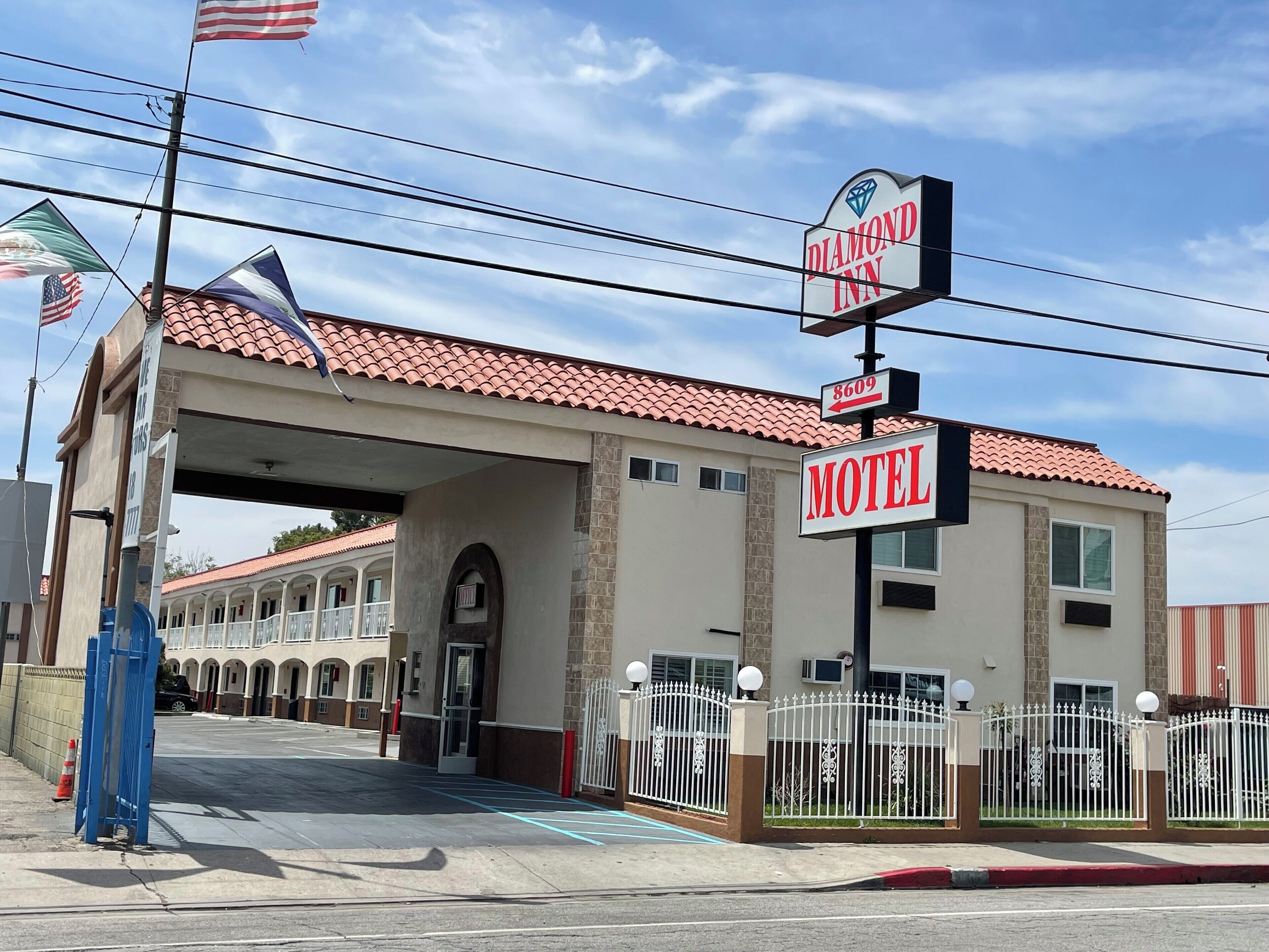 Un motel con techo de tejas rojas, un letrero que dice 'Diamond Inn' y 'Motel', y una entrada con portón.