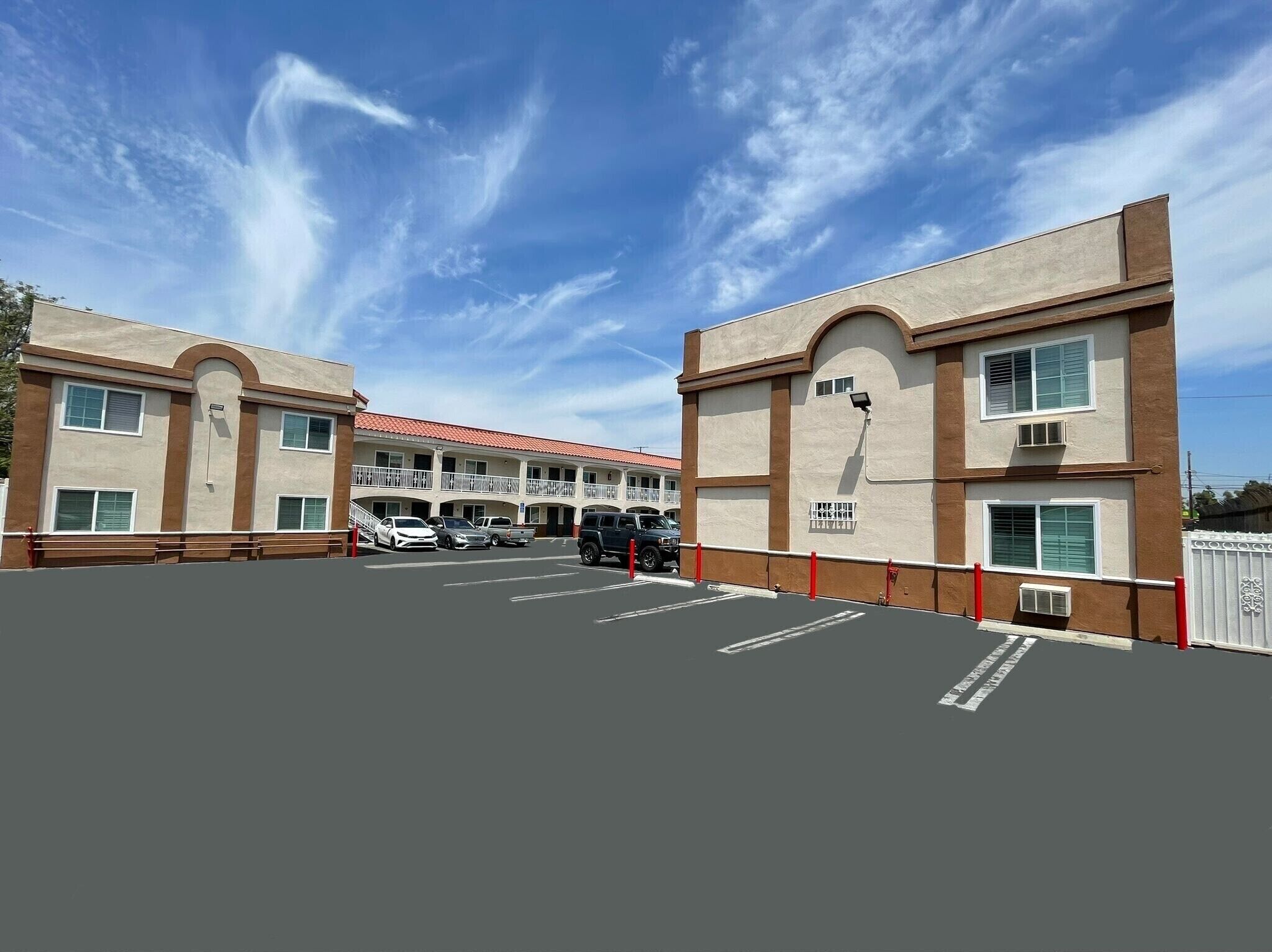A two-story building with a red-tiled roof, a parking lot, and a clear blue sky.