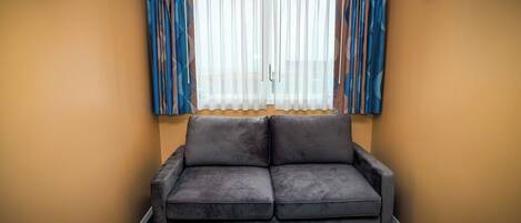 A room with a grey sofa, a window with sheer curtains, and a picture frame on the wall.