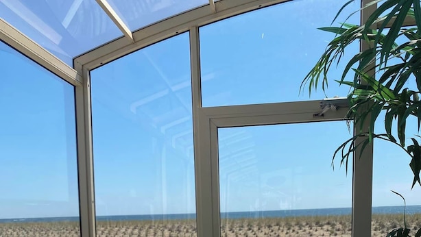 A deck with a view of the beach, a chair, a table with menus, and a plant. - The White Sands Oceanfront Resort & Spa (Point Pleasant Beach)