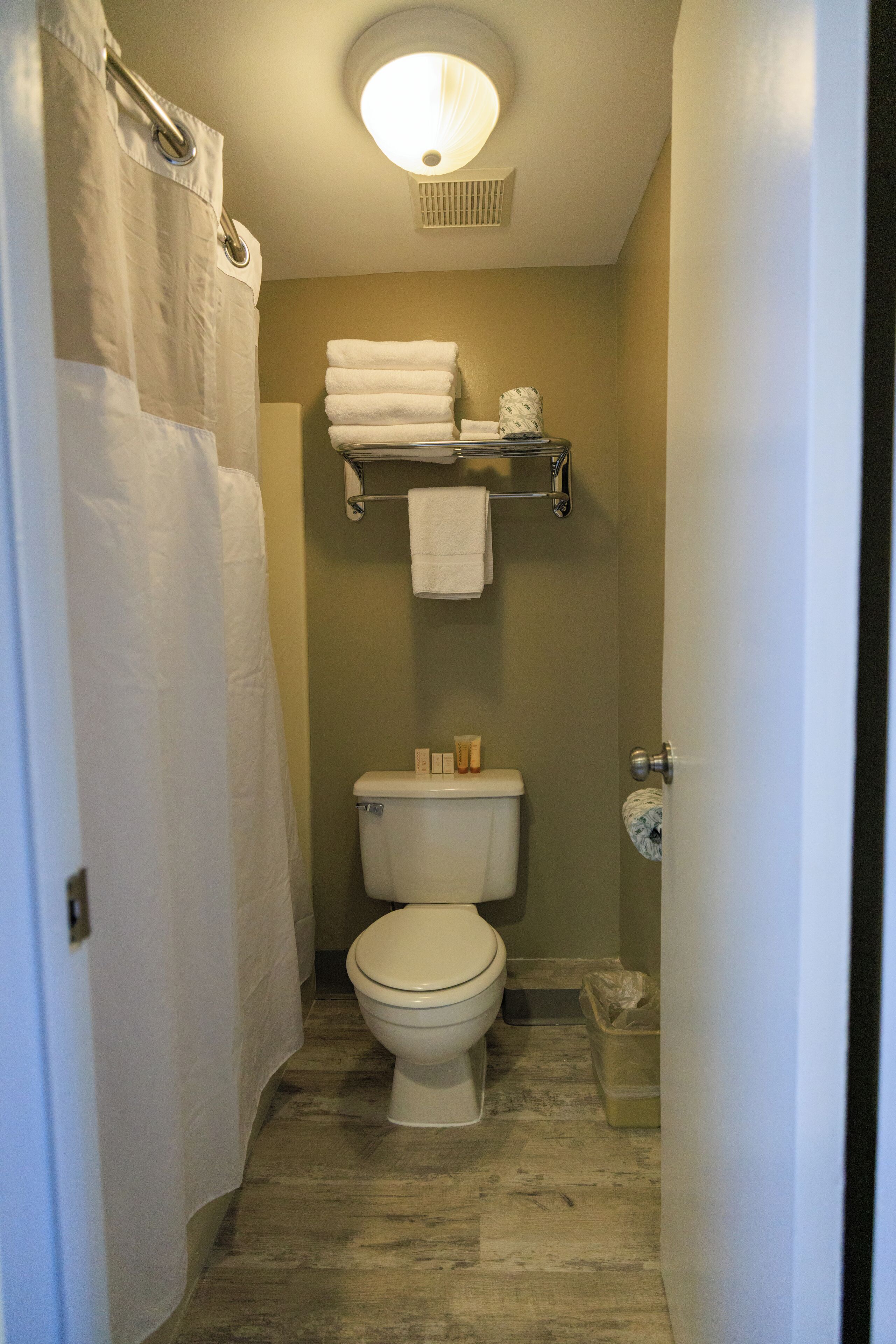 A narrow bathroom with a toilet, a towel rack, and a shower curtain.