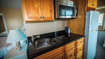 A compact kitchen with wooden cabinets, a stainless steel microwave, a built-in oven, a sink, and a white refrigerator.