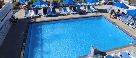 A swimming pool with blue umbrellas and lounge chairs.