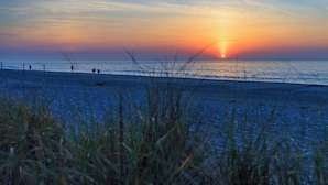 A beach with a sunset, grass in the foreground, and a few people in the distance. - The White Sands Oceanfront Resort & Spa (Point Pleasant Beach)