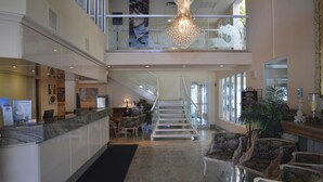 A hotel lobby with a marble reception desk, a staircase, and a chandelier. - The White Sands Oceanfront Resort & Spa (Point Pleasant Beach)