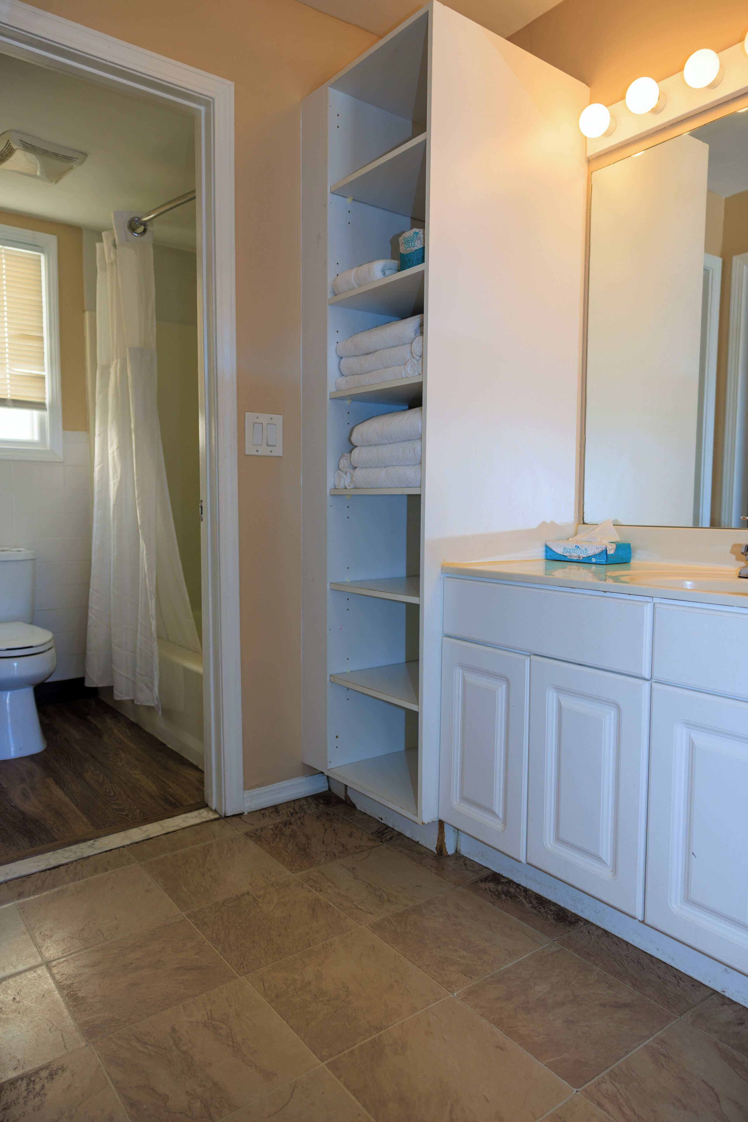 Une salle de bain avec un meuble-lavabo blanc, un miroir avec éclairage intégré et un espace douche.