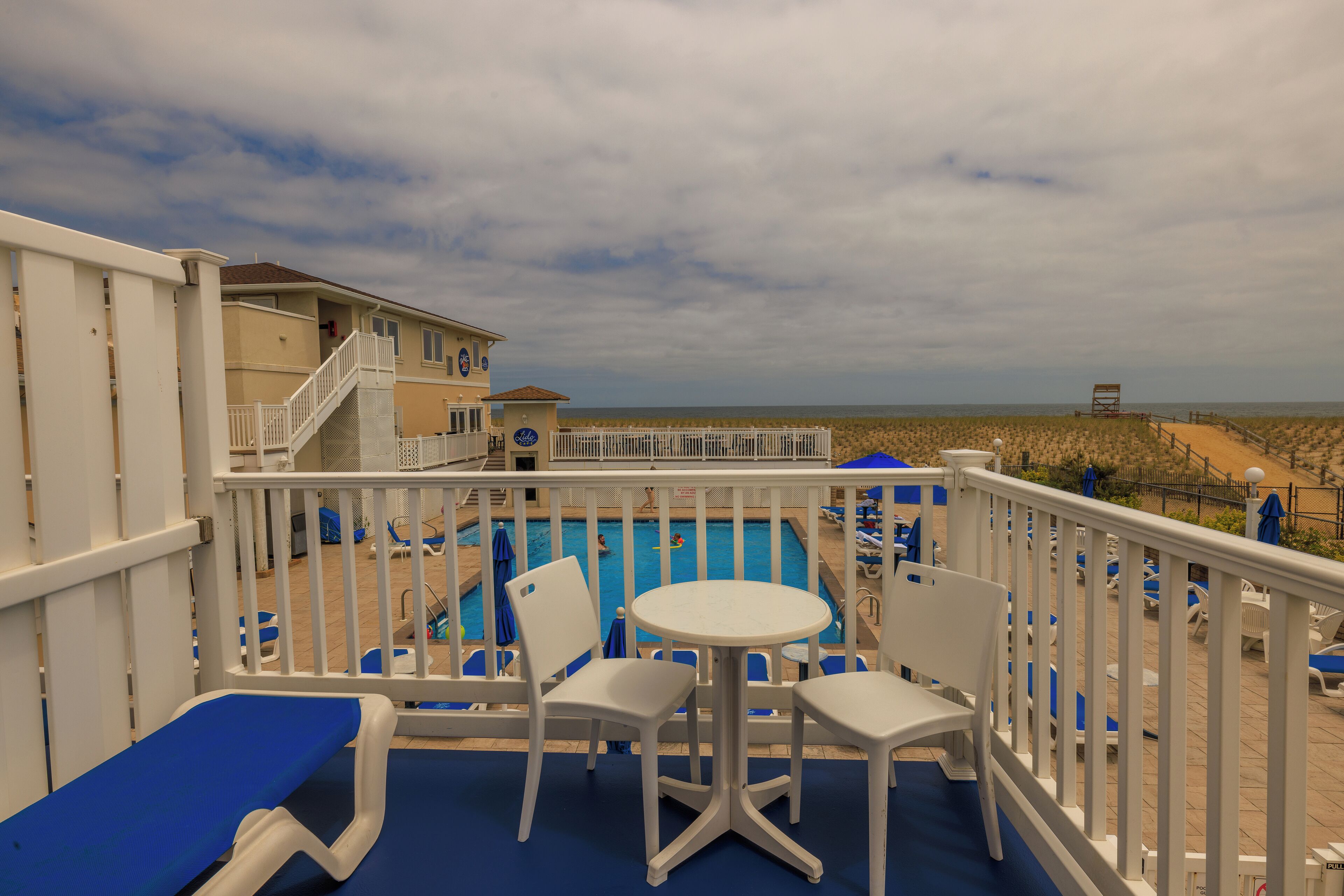 A pool area with lounge chairs and a table, overlooking a beach.