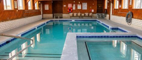 An indoor swimming pool with wooden walls, tiled flooring, and clear water.