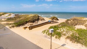A beach with a wooden walkway, dunes, and a wooden structure with a sign. - Blue Heron Motel (Nags Head)