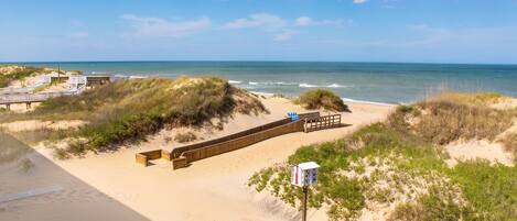 A beach with a wooden walkway, dunes, and a wooden structure with a sign.