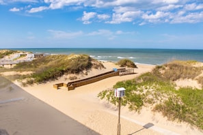 A beach with a wooden walkway, dunes, and a wooden structure with a sign. - Blue Heron Motel (Nags Head)