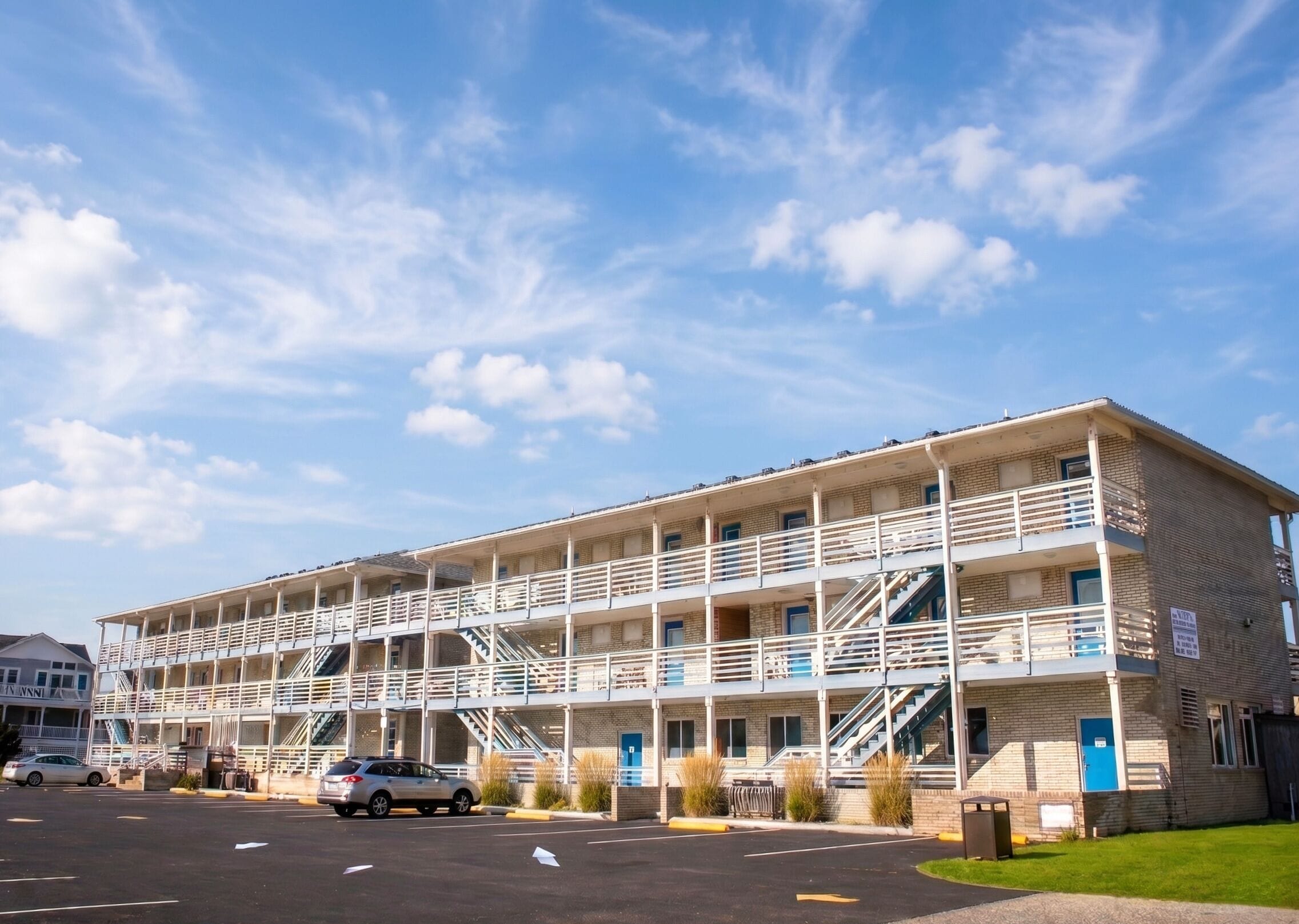 A multi-story motel with a central atrium, outdoor parking, and a clear sky.