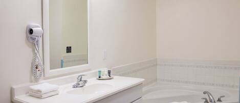 A bathroom with a white sink, a mirror, a hairdryer, a bathtub, and a towel.