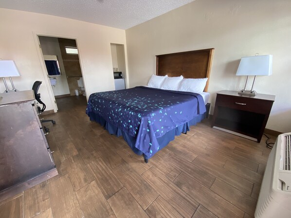 Une chambre d’hôtel avec un grand lit, un bureau, une chaise, une commode et une petite kitchenette.