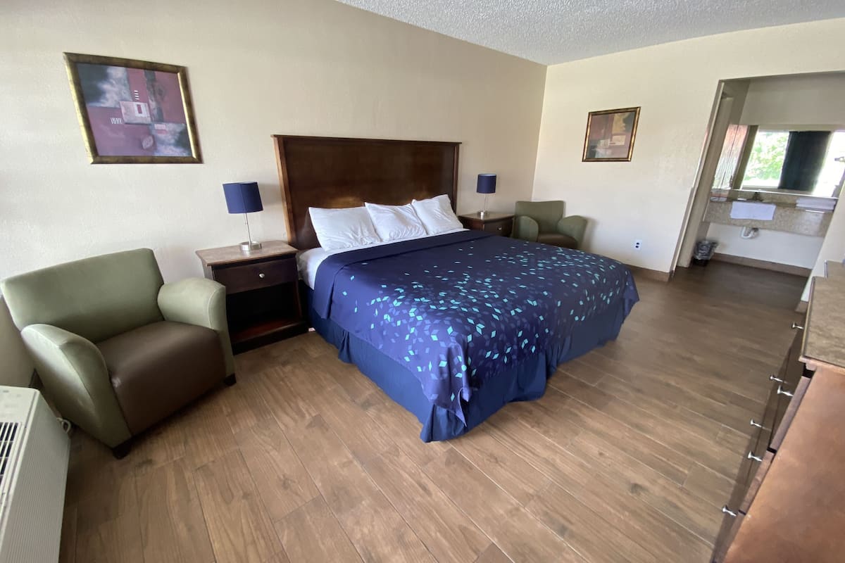 A hotel room with a large bed, a nightstand, a green armchair, and a wooden floor.