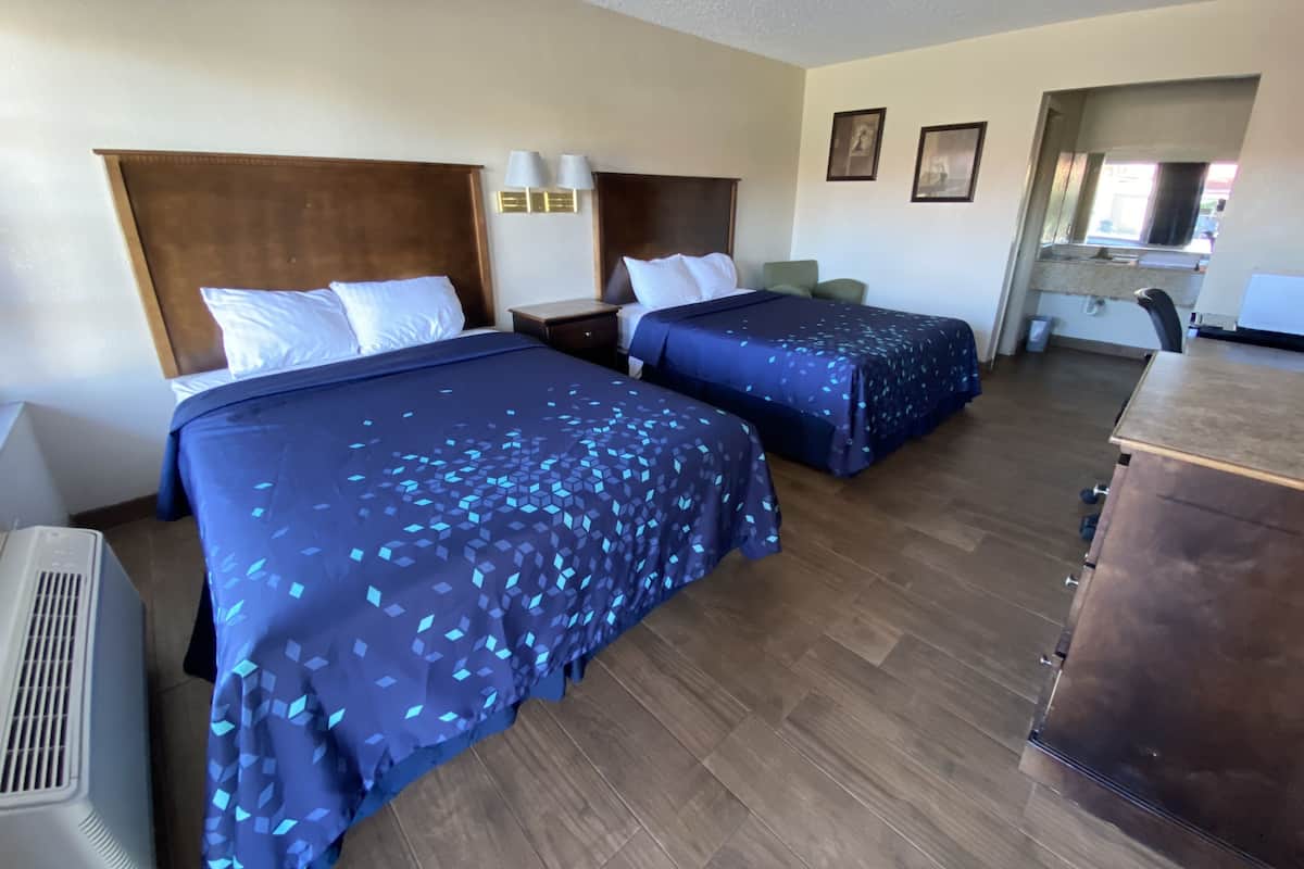 A hotel room with two beds, a desk, and a chair.