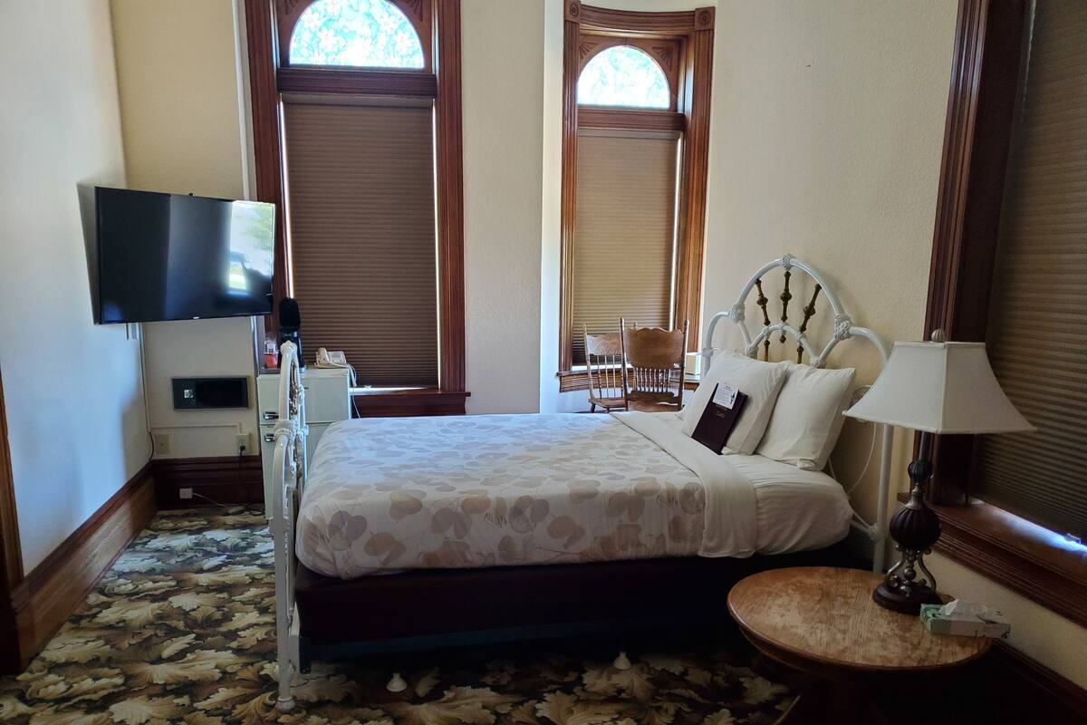 A hotel room with a bed, a bedside table, a lamp, a TV, and a chair.