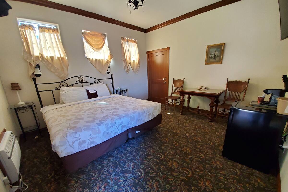 A hotel room with a bed, a desk, a chair, a radiator, and a door.