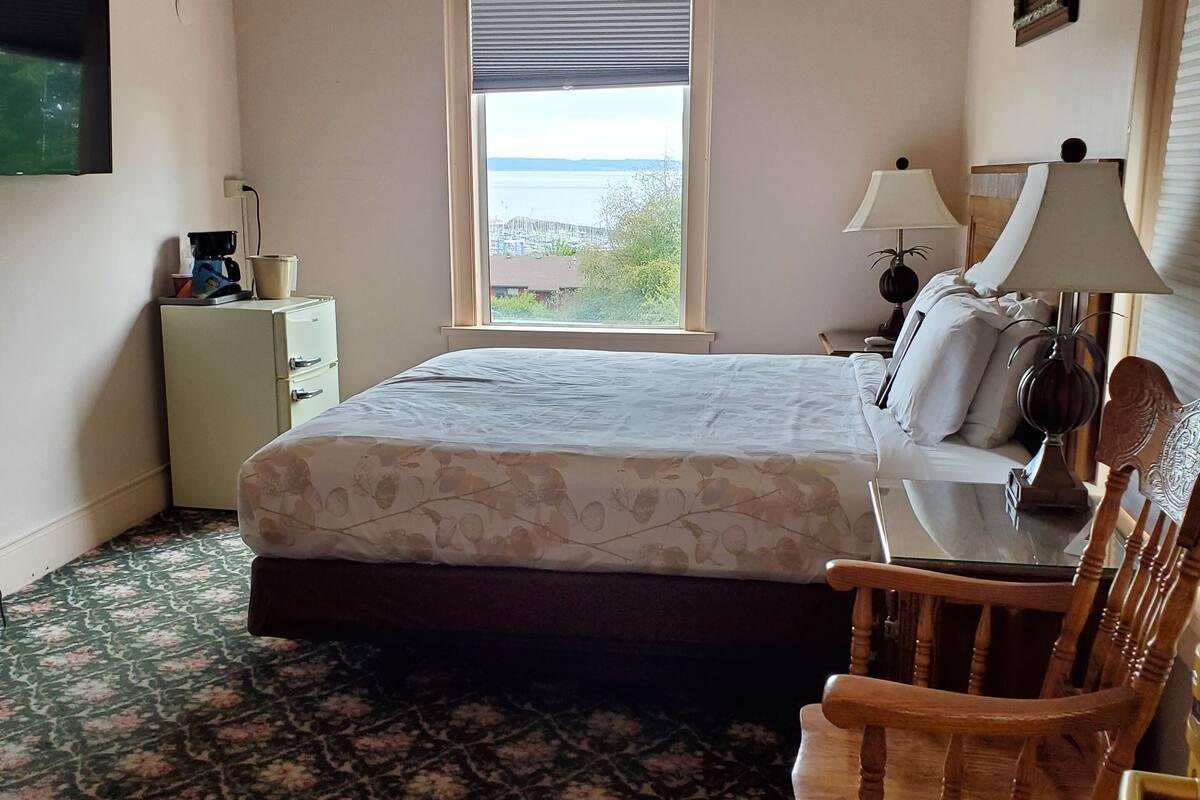 A bedroom with a bed, a chair, a desk, a lamp, a television, and a window with a view.
