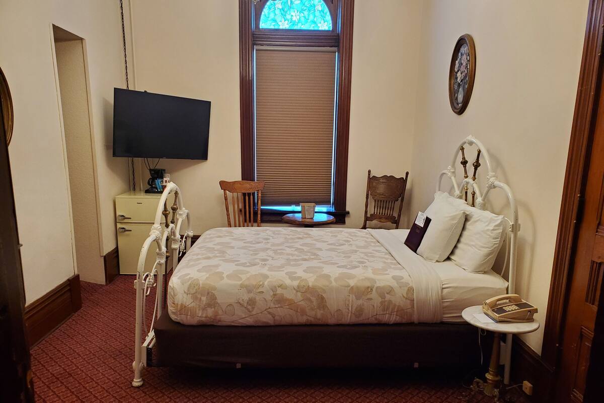 A neatly arranged bedroom with a bed, bedside table, chair, and a television on a cabinet.