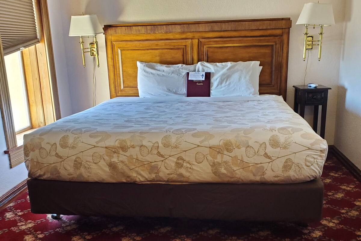A neatly made bed with a floral-patterned bedspread, a wooden headboard, and two bedside lamps.