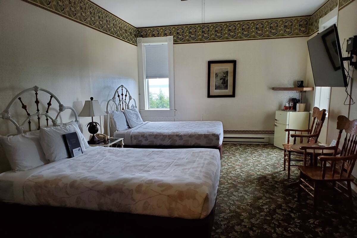 A hotel room with two beds, a desk, a chair, a television, and a window with blinds.